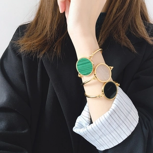 Gold open bangles with malachite and quartz stones worn over blue striped shirt