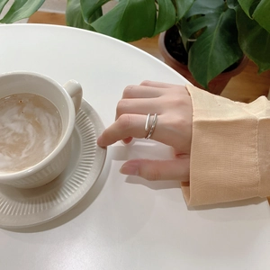 Close-up of a minimalist silver open geometric ring worn by a model in a cozy lifestyle setting
