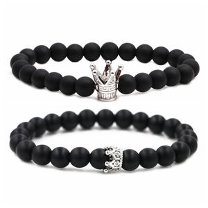 Dettaglio di bracciali con perle nere opache e ciondoli a corona in argento lucido