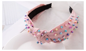 Detail of pink knotted headband featuring colorful faux pearls on a fabric surface