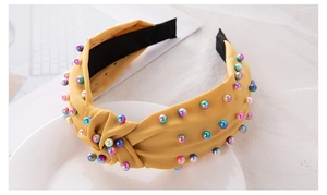 Detail of yellow fabric knotted headband decorated with colorful pearls on a white plate