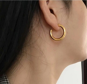 Close-up of thick gold-plated C-shaped hoop earrings worn on a model's ear