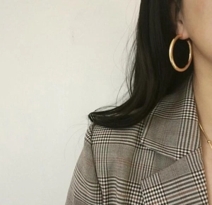 Detail of large gold hoop earring with polished finish on model in checkered suit