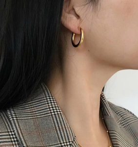 Close-up of golden round hoop earrings worn by a model in a retro plaid blazer