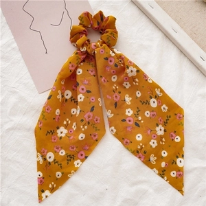 Detail of yellow floral hair scrunchie with ribbons on minimalist white fabric background