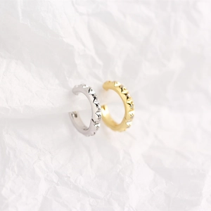 Macro shot of silver and gold C-shaped ear cuffs with sparkling diamond accents