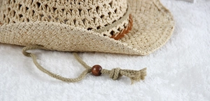 Detail of hollow woven straw hat with brown leather band and adjustable drawstring