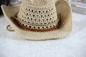 Close-up of a beige hollowed-out straw cowboy hat with a brown woven leather decorative band