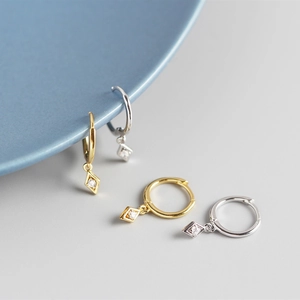 Macro shot of gold and silver geometric diamond-shaped earrings with zircon pendants