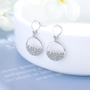 Silver circular stud earrings with cubic zirconia stones shown on white ceramic plate