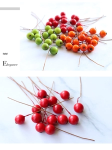 Detail of red green and orange artificial berries with wire stems on marble background