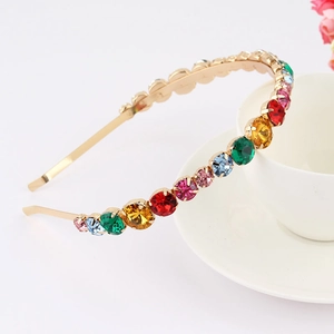 Close-up of golden headband featuring multicolored rhinestones on an ivory background