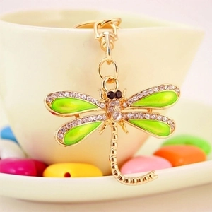 Golden dragonfly keychain with green enamel wings and crystals on a white ceramic cup