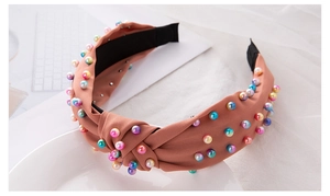 Detail of pink knotted fabric headband with multi-colored pearls on a white plate
