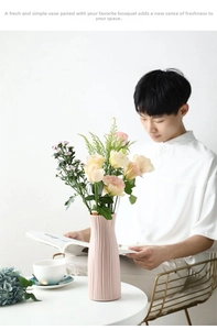 Détail d'un vase en céramique rose mat à rayures verticales sur une table blanche moderne