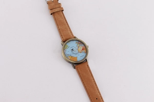 Detail view of quartz watch featuring world map dial with airplane hand and brown strap
