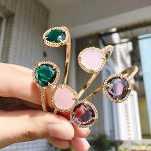 Detail of three open bangles with emerald, pink, and purple pear-shaped crystals