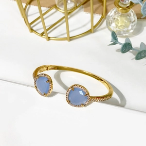 Detailed macro of golden open bangle with pear-cut light blue crystal and zircon accents