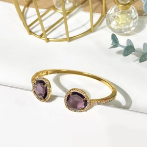 Close-up of golden bangle with two purple pear-shaped gemstones and crystal accents
