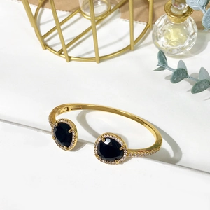 Close-up of golden open cuff bracelet with black oval stones and zircon accents