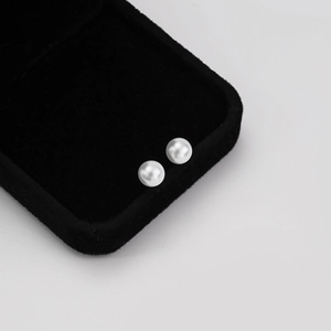 Detailed close-up of glossy white round pearl earrings set on black velvet jewelry box