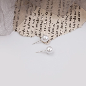 Detail shot of classic white pearl earrings with S925 silver studs on vintage newspaper