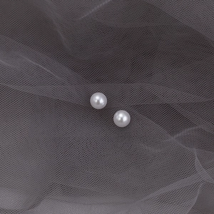 Macro shot of elegant white round pearl earrings on a premium grey lace textured background