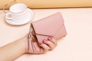 Close-up of pink tri-fold wallet with heart charm and leather tassel held in hand