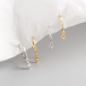 Close-up of geometric rhombus charm earrings with round zircon stones in gold and silver