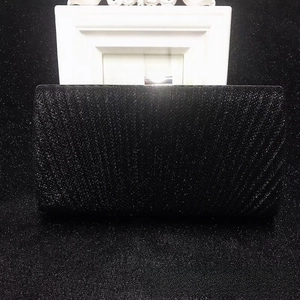 Detail of black glitter evening clutch featuring a rectangular metal clasp and hard shell