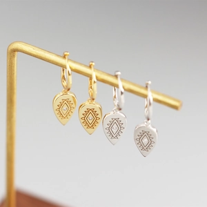 Macro detail of gold and silver teardrop earrings with geometric engravings and zircons