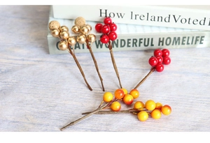 Detailed view of artificial red and gold berries on a light wood surface with books