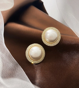 Close-up of vintage gold pearl earrings with shimmering zircon halo on silk background
