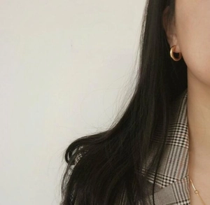 Close-up of golden hoop earrings worn by a model in a brown checkered blazer