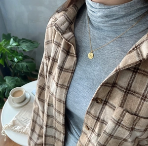 Macro shot of gold flower pendant necklace styled with casual plaid shirt layer