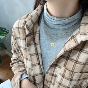 Detail of vintage gold round rose pendant necklace worn with casual checkered shirt