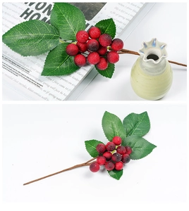 Close-up of artificial red berry stem with frosted texture and green leaves for Christmas decor