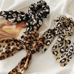 Three leopard print satin scrunchies with long ribbons on white textured fabric