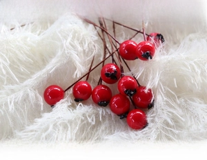 Close-up of artificial red berries with glossy finish on a white plush surface