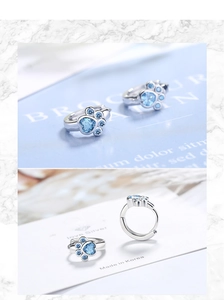 Macro detail of silver cat paw earrings with heart-shaped light blue cubic zirconia
