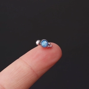 Mini stainless steel stud earring with blue opal stone shown on a fingertip