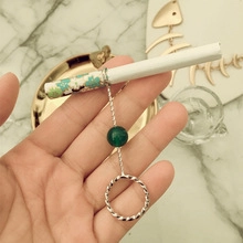 Close-up of silver rose cigarette holder ring with green bead on marble background