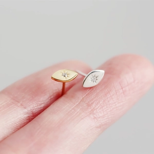 Macro shot of minimalist silver eye stud earrings with tiny zircon on a fingertip