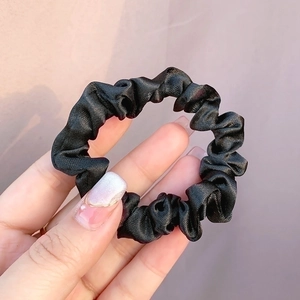 Detail of a shiny black satin scrunchie showing fabric texture and elastic stretch