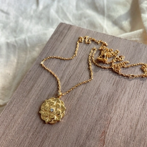 Close-up of golden floral pendant with central zircon on a fine chain over wooden texture
