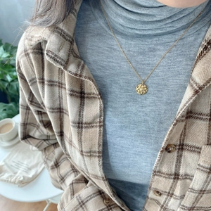 Detail of a gold flower necklace with crystal pendant on a model wearing casual clothes