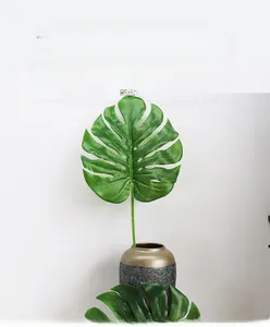Close-up of artificial monstera leaf with realistic holes in a rustic ceramic vase