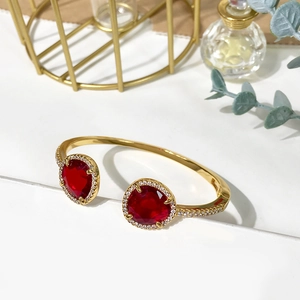 Detailed close-up of golden open bangle with red stones and micro-pave white crystals