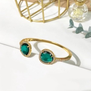 Macro detail of a gold open bangle with green teardrop stones and white diamonds