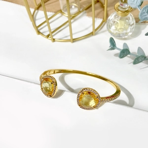 Detailed close-up of golden open bracelet with large yellow gems and micro diamonds inlay